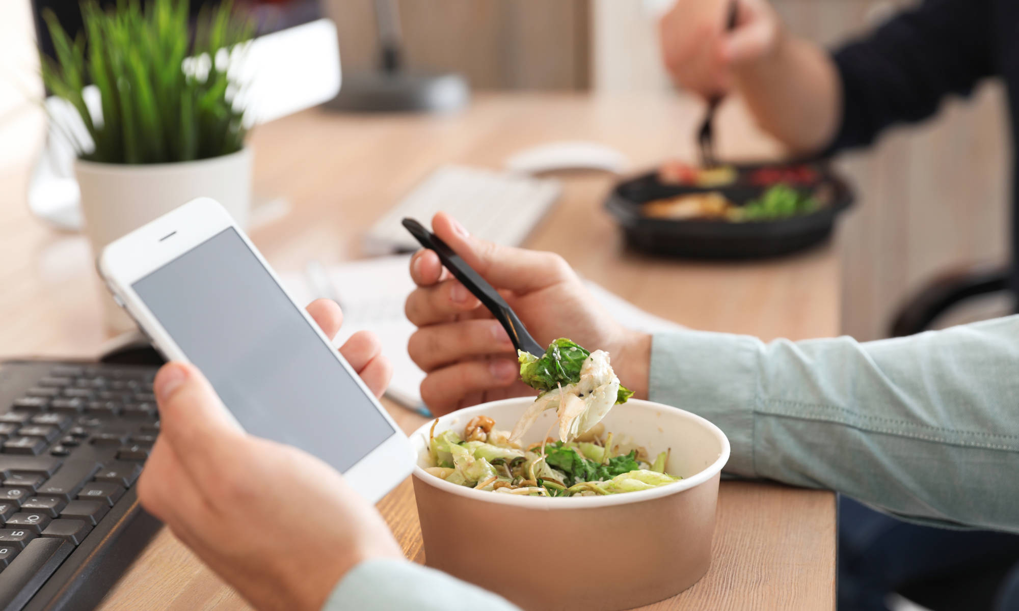 Office employee with smartphone having lunch at workplace, closeup. Food delivery