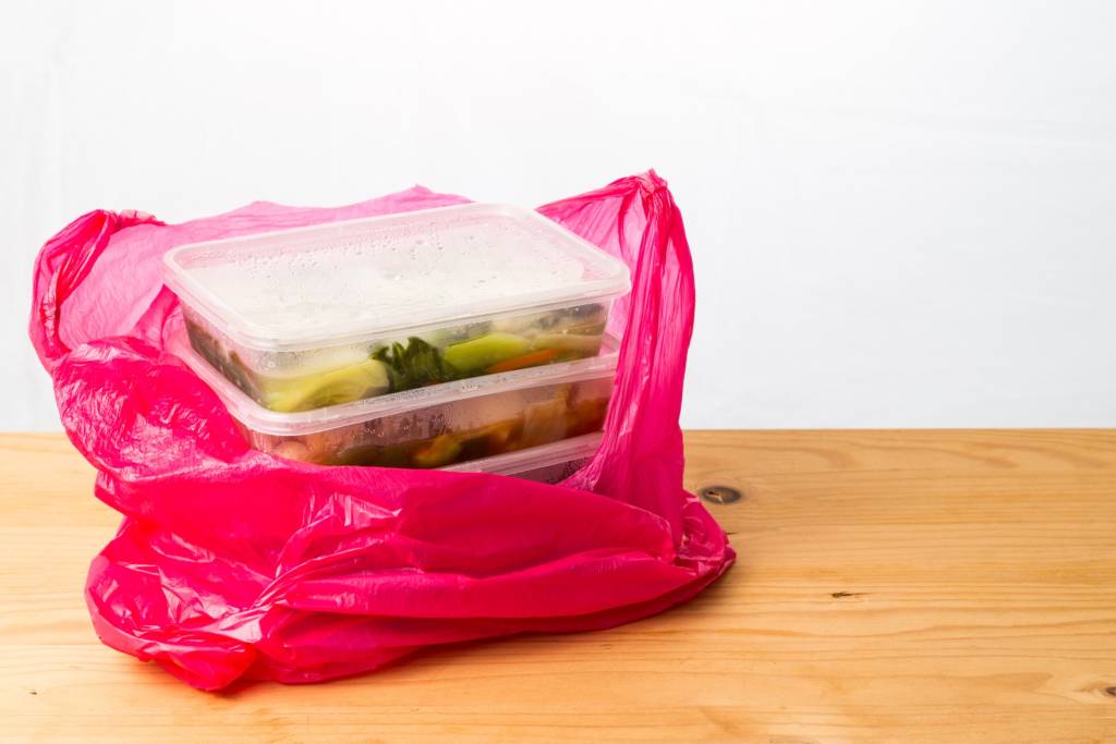 Convenient but unhealthy disposable plastic lunch boxes with take away meal in plastic bag on wooden table