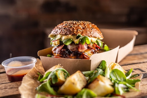 Tasty homemade burger takeaway in a box of recycled paper on wooden boards.